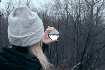 Woman looking through a glass ball in the forest on a cold winters day