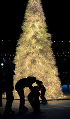 Silhouettes of people skating in front of lit Christmas Tree on cold winter day