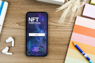 NFT (Non-Fungible Token) Marketplace app on the smartphone screen on the wooden table. Office environment