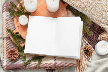 Opened book with blank pages, burning candles and winter decor on plaid
