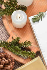 Wooden tray with burning candles, pine cone, fir tree branches and books on plaid, closeup