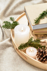 Obraz na płótnie Canvas Wooden tray with burning candles, fir tree branches and books on plaid