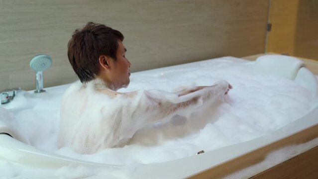 young man washing body with foam in bathtub
