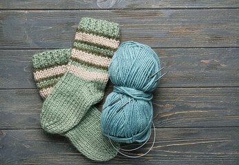 Pair of knitted socks, yarn and needles on dark wooden background