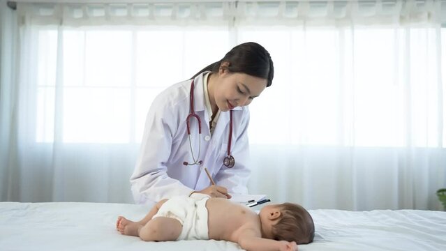 Asian woman who is a pediatrician Health check of sick newborn baby lying on white bed in hospital examination room