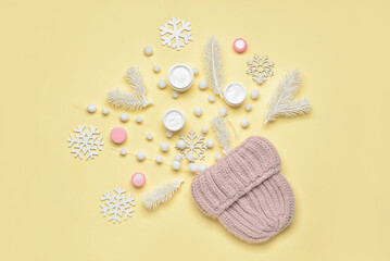 Winter composition with knitted hat, jars with cream and decor on color background
