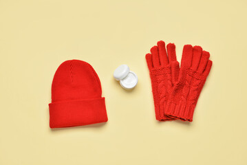 Knitted hat, gloves and jar with cream on color background