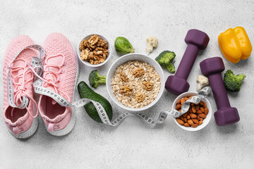 Bowls with healthy food, sneakers, dumbbells and measuring tape on light background. Diet concept