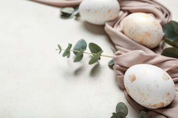 Beautiful Easter eggs, cloth and eucalyptus branches on light background, closeup