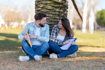 Fototapeta premium two happy students celebrating final exams result pointing fingers sitting in park