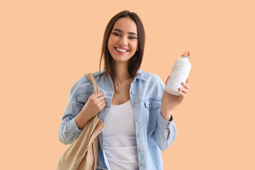 Young woman with eco bag and bottle on beige background