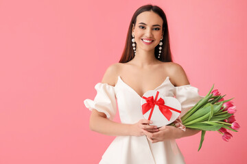 Stylish young woman with tulips and gift box on pink background. International Women's Day
