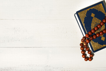 Koran and Muslim prayer beads on white wooden background