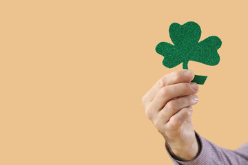 Senior man with clover on beige background, closeup. St. Patrick's Day celebration
