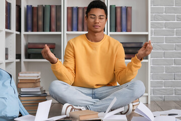 Male African-American student doing lotus pose among books in library