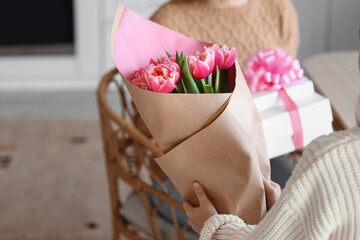 Little girl greeting her mother with bouquet of tulips in kitchen on International Women's Day,...