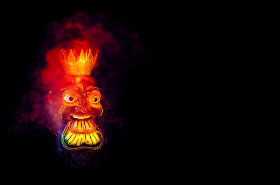 Beautiful mask of a traditional feast, surrounded by colorful smoke, with black background and copy.