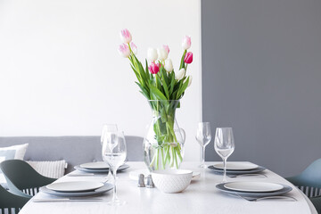 Dining table with bouquet of tulips served for International Women's Day celebration in light room...