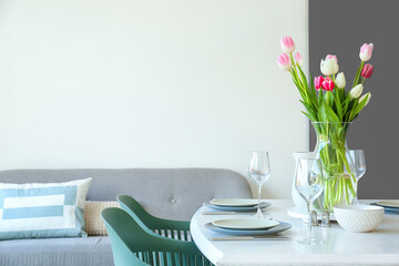 Setting and vase with tulips on dining table in room