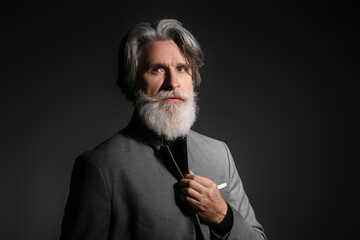 Portrait of handsome mature bearded businessman on dark background