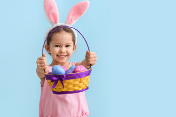 Funny little girl with bunny ears and Easter basket on blue background