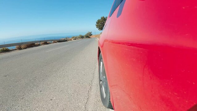 Red car speeds down scenic switchback road running through the idyllic curve mountain road. Sport car drive a challenging serpentine route leading through the stones in Greece. 