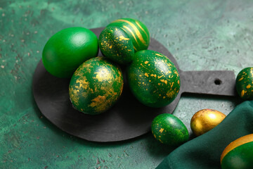 Board with stylish Easter eggs on green background
