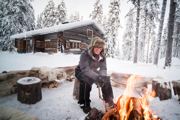 Person sat at a camp fire warming himself on a freezing cold day in winter in the Arctic Circle in Lapland, Finland