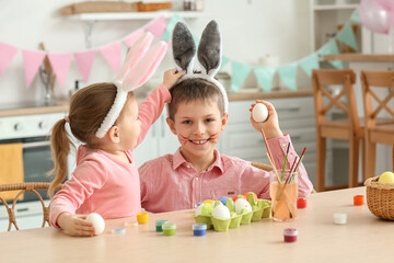 Fototapeta premium Cute little girl in bunny ears with her brother painting Easter eggs at home