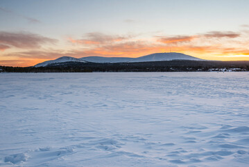 Cold weather and snow covered icy winter landscape with dramatic sunset sky and clouds over a frozen lake inside the Arctic Circle in Lapland in Finland
