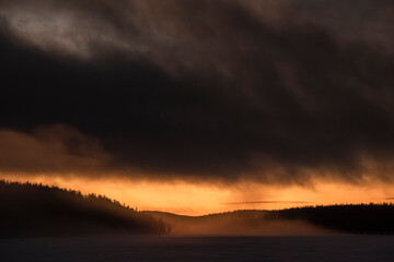Dramatic stormy clouds at sunset over a forest and frozen lake in Lapland, inside teh Arctic Circle in winter, background with copy space