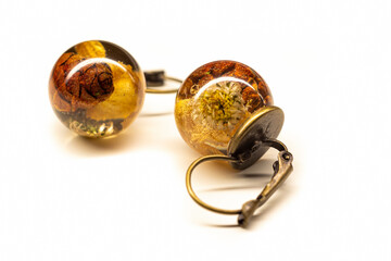 Resin earrings with natural dried plants. Bronze base, sphere ball rings, withered flowers and tree cones. Selective focus on the details, object isolated on white background.