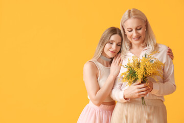 Young woman with her mother and mimosa flowers on yellow background