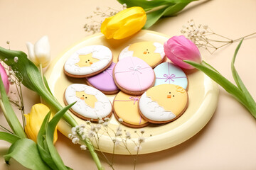 Obraz na płótnie Canvas Plate with creative Easter cookies and flowers on beige background, closeup