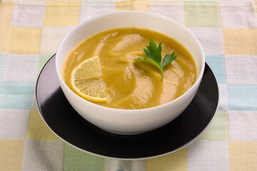 Vegetable soup puree with parsley and lemon in a white cup is on a colored napkin