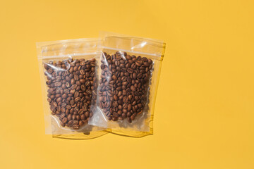Roasted arabica coffee beans in blank transparent plastic bag with zipper on yellow background....