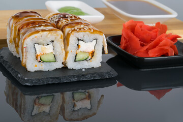 on a black table with a reflection, eel rolls and ginger flavor seasoning, close-up