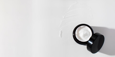 An open jar of skin moisturizer on a smear of white cream. The concept of natural cosmetics. Copy space.