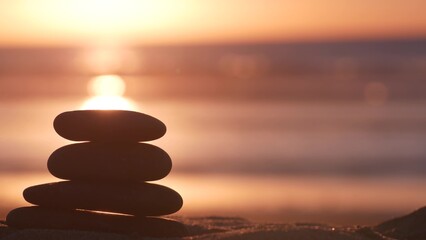 Stack of pebble stones, sandy ocean beach, sunset sky. Rock balancing in sun light, sea water waves. Stones staking in pyramid pile. Zen meditation and harmony in balance. Seamless looped cinemagraph.