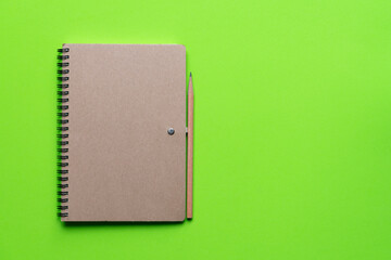 Notebook with a wooden pencil on green background, close up