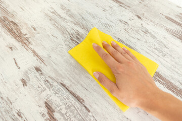 One hand is wiping the surface of a tile with a yellow square shaped cloth and copy space