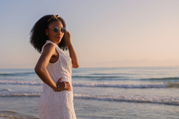 Woman wearing sunglasses on the beach in summer clothes looking back at the camera