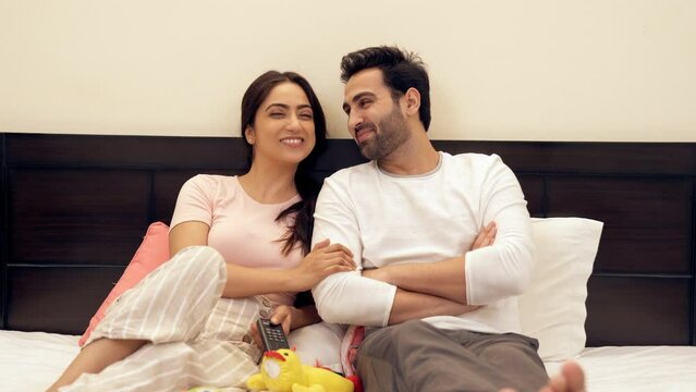 Happy cheerful couple watching their favorite program together on television. An Indian young man and his pretty wife spending time together - leisure time  healthy partnership  less stress  date n...