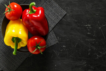 Tomatoes and peppers sweet bulgarian whole, on gray round plate on dark tablecloth and background, top view, with space to copy text.