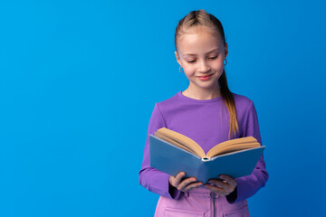 Little beautiful smiling girl holding book against blue background