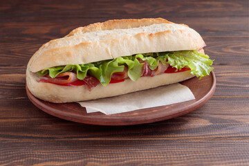 Close-up view of The banh mi sandwich with sliced grilled pork and peppers and salad packed in paper on plate on wooden background. Selective focus.
