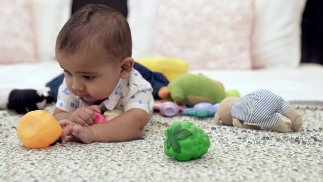 A sweet little baby boy learning to crawl lying down alone in the modern bedroom. An adorable infant playing with his colorful soft toys in his leisure time - creativity and imagination  developing...