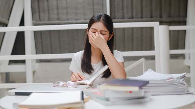 Asian student women read books in library at university. Young undergraduate girl stress tired have problem while study hard for knowledge on lecture desk at college campus concept.
