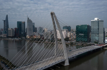 Drone view of city center and large cable-stayed  suspension bridge over river with blue sky. Location is Ho Chi Minh City and Thu Thiem Bridge in Vietnam.