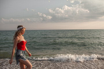 Beautiful strong woman with short hair wearing  red swimming suit and shorts walking in the beach against the blue sky and sea